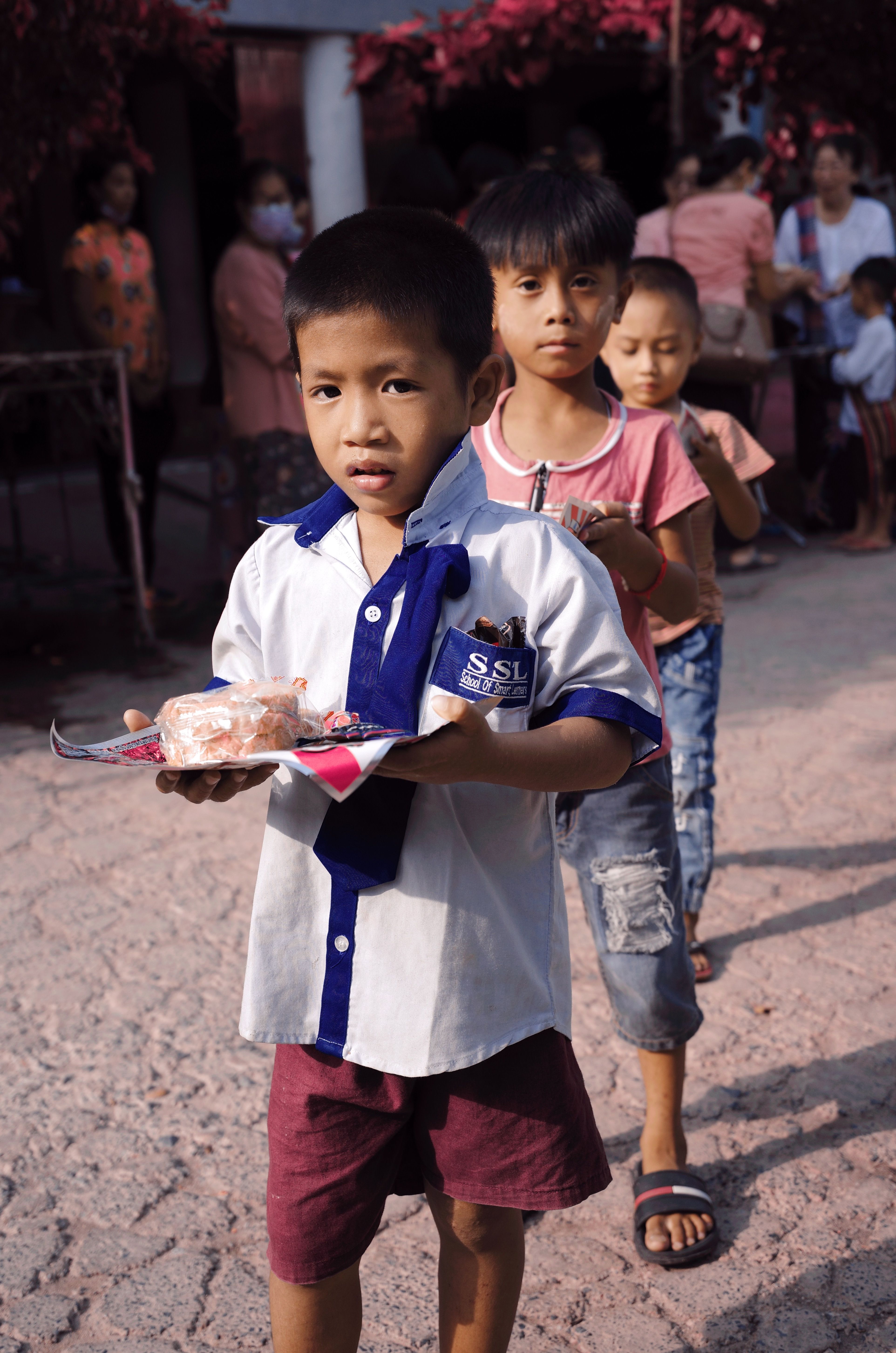 Children standing together outdoors, with a child holding food in the foreground